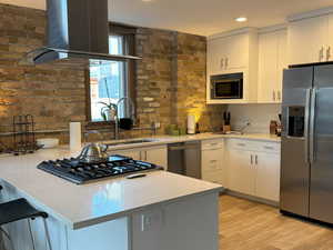 Kitchen with a peninsula, stainless steel appliances, island exhaust hood, white cabinetry, and light wood-style floors
