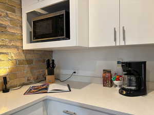 Kitchen view of light stone countertops, white cabinetry, stainless steel microwave, and modern cabinets