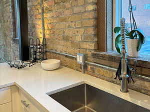 Kitchen featuring light stone countertops, white cabinetry, and brick wall