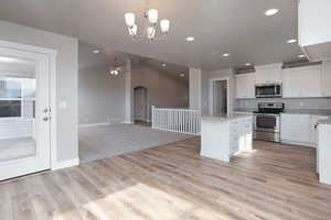 Kitchen with white cabinetry, open floor plan, pendant lighting, stainless steel appliances, and a kitchen island