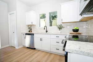 Kitchen with range hood, white cabinetry, and light stone countertops