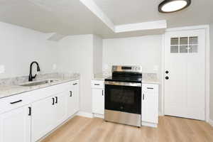 Kitchen with stainless steel electric stove, white cabinets, a textured ceiling, and light wood-style floors
