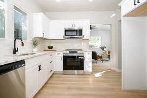Kitchen with appliances with stainless steel finishes, white cabinetry, backsplash, light wood-type flooring, and recessed lighting