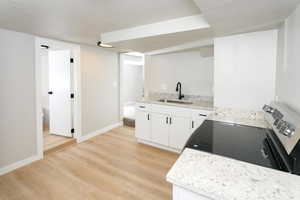 Kitchen featuring white cabinets, light wood finished floors, a textured ceiling, light stone counters, and electric range