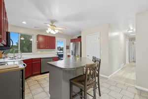 Kitchen with stainless steel appliances, dark brown cabinets, a breakfast bar area, light tile patterned flooring, and a ceiling fan