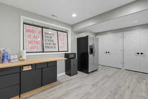 Kitchen featuring stainless steel refrigerator with ice dispenser, light wood-style flooring, wooden counters, black microwave, and recessed lighting