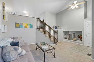 Carpeted living area with stairs, tile patterned floors, high vaulted ceiling, and ceiling fan