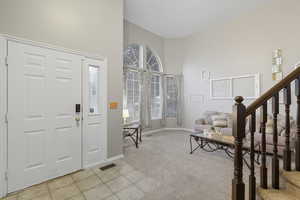 Foyer with light carpet, stairs, light tile patterned floors, and a high ceiling