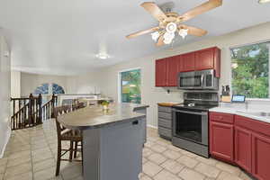 Kitchen with appliances with stainless steel finishes, a breakfast bar area, a kitchen island, ceiling fan, and light tile patterned floors