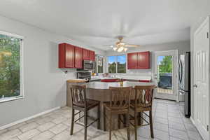 Kitchen featuring reddish brown cabinets, dark countertops, appliances with stainless steel finishes, a kitchen breakfast bar, and light tile patterned flooring
