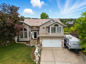 Tri-level home featuring an attached garage, brick siding, concrete driveway, and a shingled roof