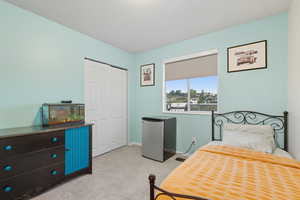 Bedroom with light colored carpet, stainless steel fridge, and a closet