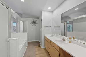 Full bathroom featuring double vanity, a bath, recessed lighting, light wood-style floors, and lofted ceiling