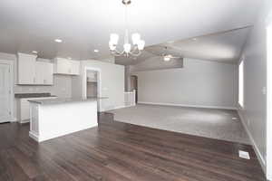 Kitchen with white cabinets, a ceiling fan, vaulted ceiling, hanging light fixtures, and a chandelier
