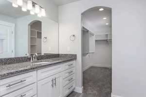Bathroom with a walk in closet, vanity, recessed lighting, and dark colored carpet