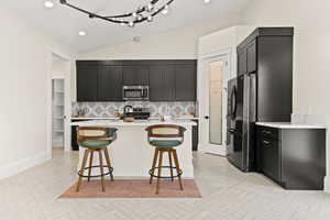 Kitchen with dark cabinetry, tasteful backsplash, appliances with stainless steel finishes, a breakfast bar, and light stone counters