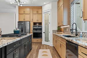 Kitchen with light stone counters, stainless steel appliances, wood tiled floors, light brown cabinetry, and recessed lighting