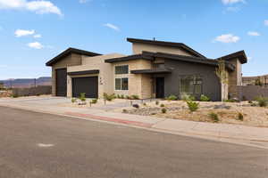 View of front of property with stucco siding, driveway, stone siding, a garage, and a mountain view