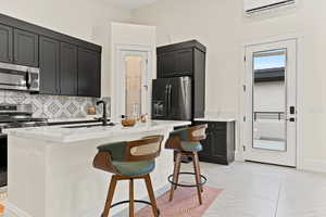 Kitchen featuring a kitchen breakfast bar, light stone countertops, stainless steel appliances, backsplash, and dark cabinetry