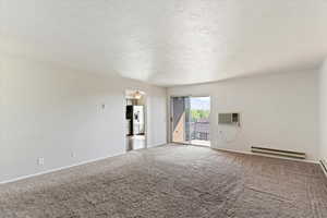 Carpeted empty room featuring a textured ceiling, a baseboard radiator, and a wall mounted AC