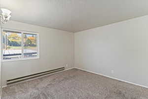 Carpeted spare room with baseboard heating and a textured ceiling