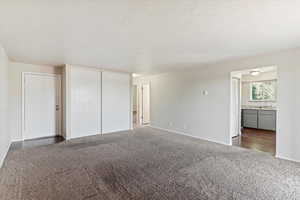 Unfurnished bedroom with a closet, carpet, a textured ceiling, and ensuite bath