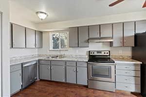 Kitchen with appliances with stainless steel finishes, gray cabinetry, light countertops, dark wood-style flooring, and under cabinet range hood