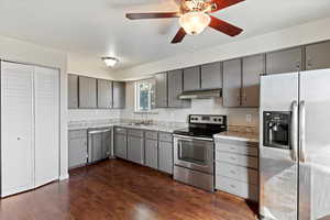 Kitchen featuring appliances with stainless steel finishes, light countertops, dark wood-style flooring, a ceiling fan, and under cabinet range hood