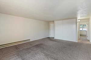 Empty room featuring carpet flooring, a textured ceiling, and a baseboard heating unit
