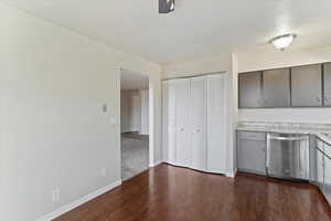 Kitchen with stainless steel dishwasher, gray cabinets, light countertops, and dark wood-style flooring