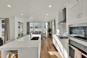 Kitchen with a kitchen breakfast bar, appliances with stainless steel finishes, white cabinetry, wall chimney range hood, and a kitchen island with sink