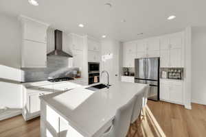 Kitchen featuring light wood finished floors, stainless steel appliances, white cabinets, decorative backsplash, and recessed lighting