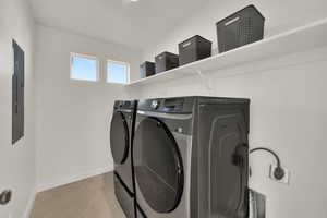 Laundry area with light tile patterned flooring, washer and clothes dryer, and electric panel