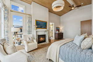Bedroom featuring wood finished floors, high vaulted ceiling, a high end fireplace, a wood ceiling with exposed beams, and a ceiling fan