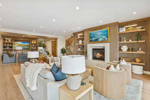 Living room featuring light wood finished floors, built in features, recessed lighting, a fireplace, and stairway