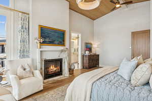 Bedroom with high vaulted ceiling, wood finished floors, a high end fireplace, ceiling fan, and a wood ceiling with exposed beams