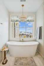Full bath featuring a soaking tub, plenty of natural light, and light marble finish floors
