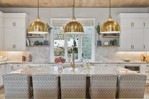 Kitchen with white cabinetry, tasteful backsplash, open shelves, light stone counters, and wood ceiling
