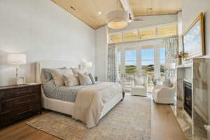 Bedroom featuring wood finished floors, a fireplace with flush hearth, wood ceiling, access to exterior, and high vaulted ceiling