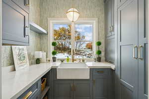 Bar with gray cabinetry, decorative light fixtures, light stone countertops, open shelves, and wallpapered walls