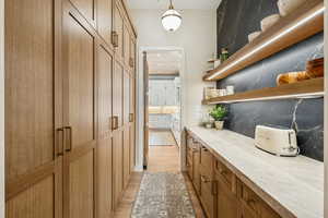 Bar area featuring brown cabinetry, open shelves, light wood-style floors, tasteful backsplash, and hanging light fixtures