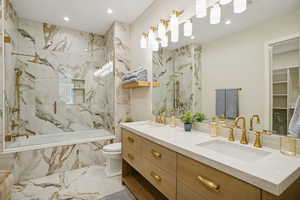 Bathroom featuring double vanity, a spacious closet, recessed lighting, light marble finish floors, and tiled shower / bath combo
