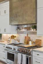 Kitchen featuring white cabinets, range with two ovens, light stone counters, backsplash, and open shelves