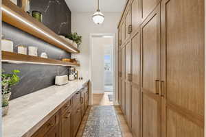 Bar area with open shelves, light wood finished floors, brown cabinets, light stone counters, and decorative light fixtures