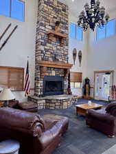 Carpeted living area with healthy amount of natural light, a stone fireplace, a chandelier, and a high ceiling