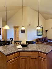 Kitchen featuring brown cabinets, open floor plan, hanging light fixtures, dark stone counters, and high vaulted ceiling