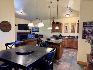Kitchen featuring hanging light fixtures, brown cabinetry, a kitchen island, dark stone countertops, and a tiled fireplace