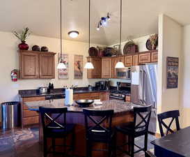 Kitchen featuring stainless steel appliances, a breakfast bar area, hanging light fixtures, and brown cabinets