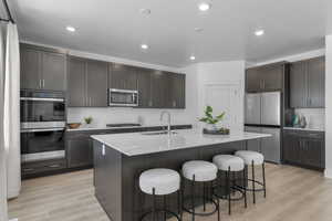 Kitchen featuring appliances with stainless steel finishes, recessed lighting, light wood-style flooring, a center island with sink, and dark brown cabinets