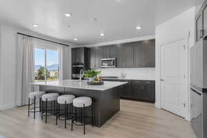 Kitchen with a breakfast bar, stainless steel appliances, a kitchen island with sink, light wood-style flooring, and recessed lighting